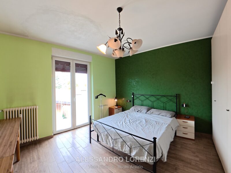 Camera da letto matrimoniale con parete verde e accesso al balcone